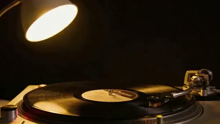 AI-generated video still: a black vinyl record turning under a warm studio lamp with light rippling across the grooves