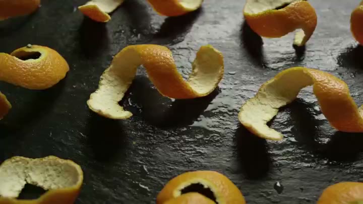 AI-generated video still: a macro view of a wet slate surface scattered with pieces of citrus peel